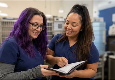 Two veterinary technicians in blue scrubs reviewing hospital policies together in a clinic setting.