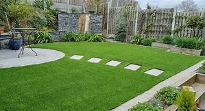 Modern backyard garden with lush green artificial grass, stone stepping stones, and a patio area.