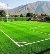 Green artificial turf soccer field with white markings and mountains in the background.