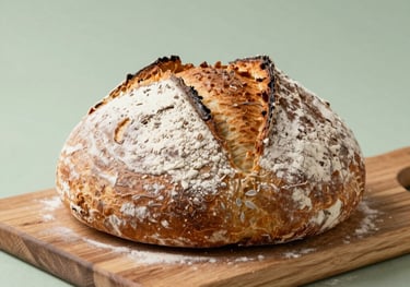 A photograph of artisan sourdough loaves with dusted flour, sitting on a wooden cutting board with a soft sage green background, North American kitchen style.