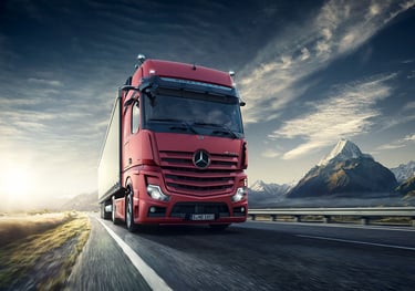 a red truck driving down a road with mountains in the background
