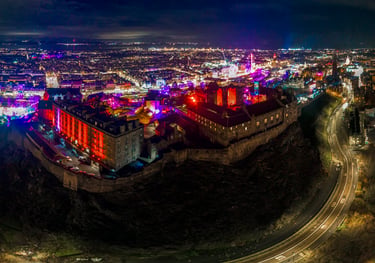 Aerial night view of Edinburgh Castle with colourful festival lights across the city and Princes Street