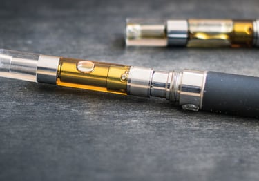 A close-up of a vape pen battery attached to a clear oil cartridge filled with amber cannabis distillate.