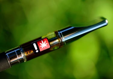 Close-up of a cannabis oil vape cartridge with a THC warning label against a blurred green background.