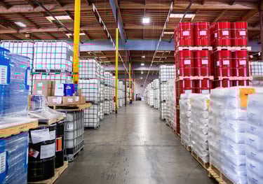 Warehouse with barrels stacked on pallets, filled with various chemicals