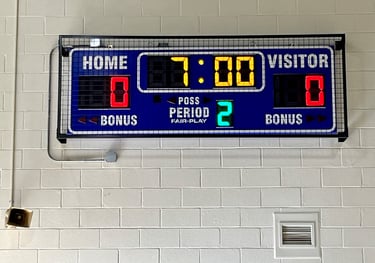 Scoreboard with protective wire mesh screen mounted on a gym wall