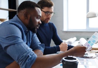 two men sitting at a desk with a laptop