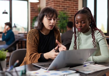 two women sitting at a table with laptops
