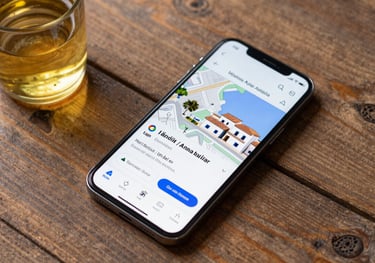 A top-down view of a smartphone on a rustic wooden table showing a Google Maps local business listing for an oil mill, glass of golden AOVE nearby, Mediterranean / Spanish / Andalusian style.