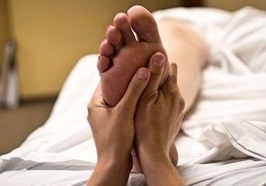 Soles of client's feet being massaged by therapist's hands while she lies on a treatment bed.