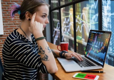 Mulher sentada a frente de computador com gráficos da bolsa de valores