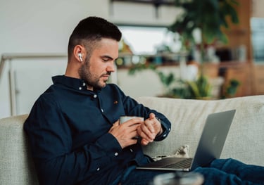 a man sitting on a couch with a laptop and a cell phone