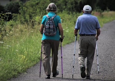 elderly senior adult male and female walking on path with walking sticks for exercise