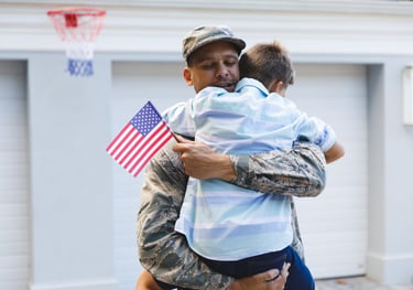 a veteran in uniform carrying his son and holding a us flag