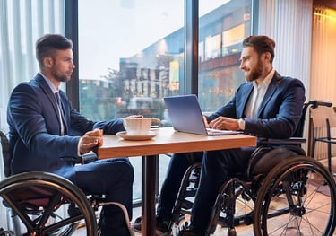 Zwei Rollstuhlfahrer sitzen für ein Beratungsgespräch in einem Café