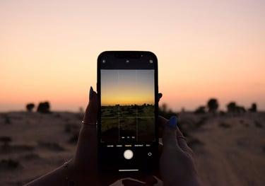 A hand holding a mobile phone in the desert at sunset