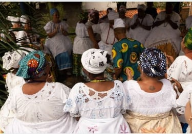 Foto de cerimônia no candomblé, com pessoas em roda, vestindo roupas brancas e turbantes coloridos.