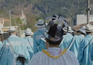 Foto de um grupo de Congado em cortejo na rua. Estão vestidos de azul e com uma pessoa coroada. 