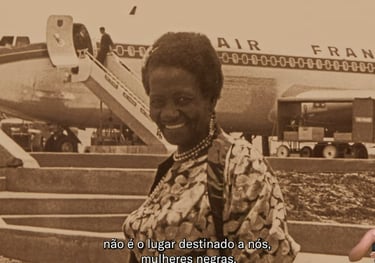 Captura de vídeo da exposição de Carolina Maria de Jesus sorrindo em frente a um avião da AIR France