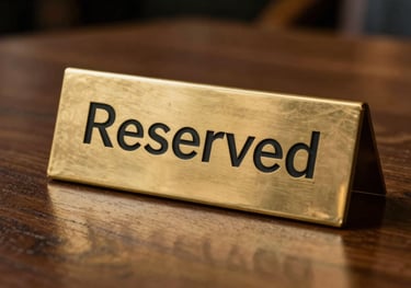 An artistic shot of a 'Reserved' sign made of polished brass on a dark wood table in an upscale restaurant. Minimalist and professional.