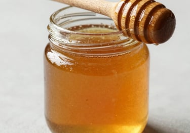 A small jar of wild forest honey with a wooden dipper, back-lit to show the deep golden amber color, elegant and clean.