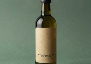 A dark glass bottle of premium cold-pressed oil with a minimalist tan label, standing in soft natural light against a dark sage green background.
