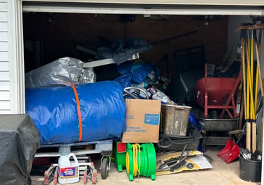 Cluttered garage storage space filled with boxes, garden tools, and a blue tarp needing organization.