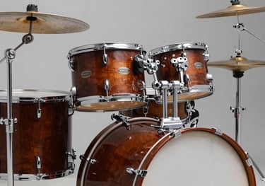 A professional drum kit in a studio, featuring polished chrome hardware and deep chestnut wood shells, captured with soft lighting.