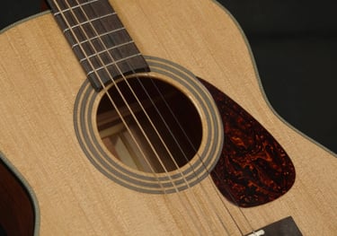 A close-up of the body of a classical acoustic guitar made of golden tan cedar wood, with intricate rosette details around the soundhole.