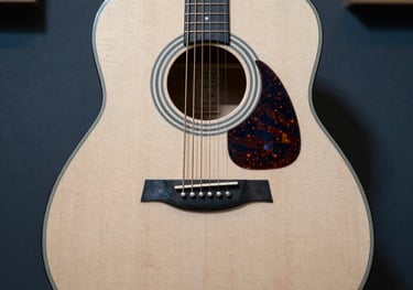 A top-down view of a modern acoustic guitar in a professional music studio, with soft light hitting the off-white wood grain and blue shadows.