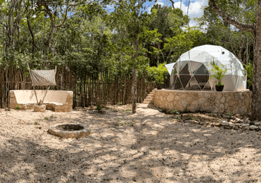 Luxury geodesic dome for glamping with fire pit and outdoor seating in a lush Mayan rainforest setti