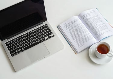 A top-down view of a South Asian / Indian student's desk featuring a laptop, a medical textbook, and a cup of tea, in a clean, minimal mist white room.
