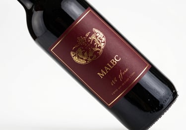 A bottle of Malbec wine with a deep burgundy label and gold laser engraving, professional studio photography on white background.