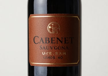 A bottle of Cabernet Sauvignon wine with a personalized leather-textured label, professional studio photography on white background.