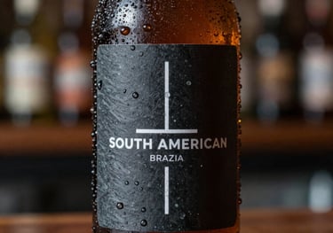 Close up of a cold craft beer bottle with drops of water, dark slate label with minimalist design, South American / Brazilian urban bar setting.