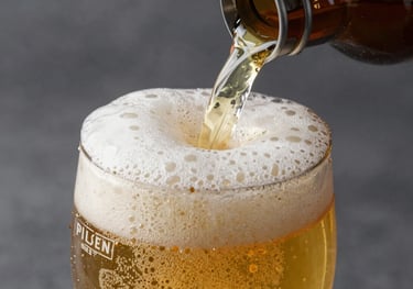 A macro shot of a crisp Pilsen draft beer being poured, golden liquid and white foam, dark slate and mist grey background.