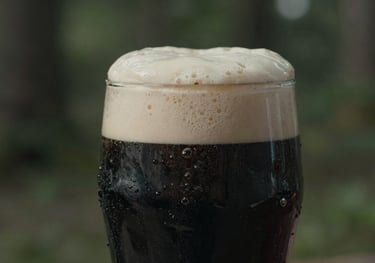 A detailed close-up of a rich, dark porter in a rustic glass, the dark slate grey liquid topped with a thick, creamy head, set against a blurred sage green forest.