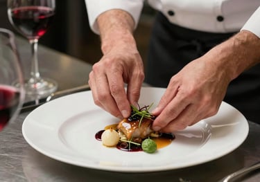 A high-angle shot of a chef's hands artfully arranging a private dining plate in a luxury kitchen, with burgundy wine accents in the background.