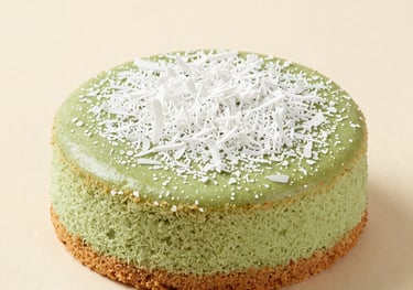 A soft green Pandan-infused cassava cake decorated with white coconut flakes. Fresh, clean composition with off-white and tan accents.