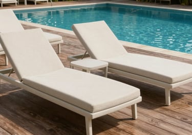 Minimalist pool loungers in a neutral off-white recycled material, arranged neatly on a wooden deck by a luxury swimming pool in a South Asian resort setting.