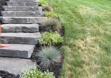 Natural stone landscape stairs curving up a green grass hillside with ornamental shrubs.