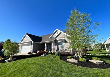 Modern ranch-style home with grey siding, professional landscaping, and a manicured green lawn under a clear blue sky.