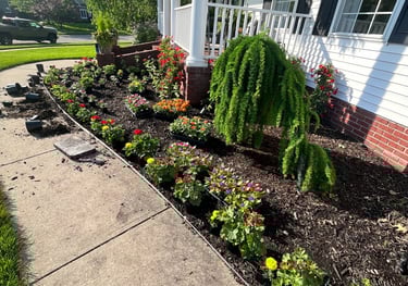 Freshly planted flower bed with colorful annuals and mulch along a white house front porch.
