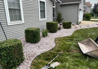 Residential landscaping project featuring curved garden edging with decorative pink stone and boxwood shrubs.
