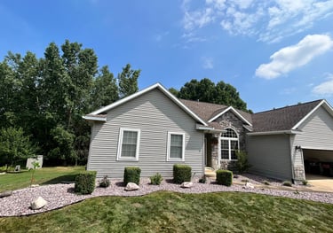 A gray ranch style house with stone accents, professional landscaping, and a manicured lawn.