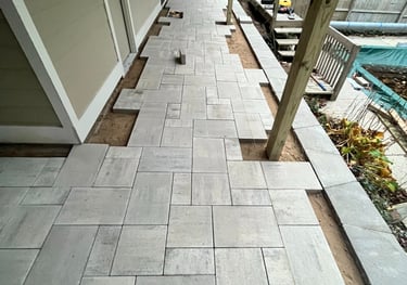 Professional installation of a modern gray stone paver patio under a residential deck.