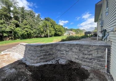 Newly installed grey stone tiered retaining wall in a residential backyard landscape.