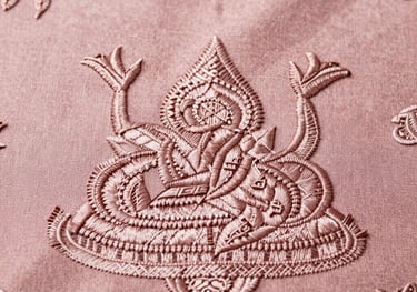 Macro shot of high-quality embroidery on a pastel dusty rose fabric. Elegant and intricate patterns inspired by traditional Southeast Asian art.