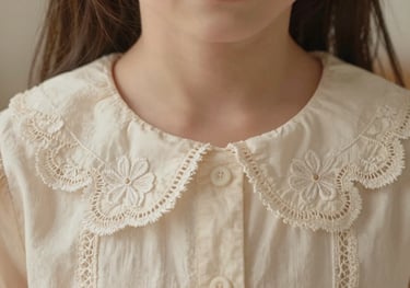 A detailed shot of a girl's dress collar with delicate lace embroidery in soft cream tones, warm and premium lighting.