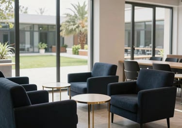 A photograph of a modern and stylish student common room at a Cyprus institute. The space features dark navy armchairs, gold-trimmed side tables, and large windows looking out onto a sun-drenched courtyard.